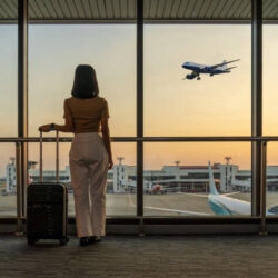 travel-tourist-standing-with-luggage-watching-sunset-at-airport-window-woman-looking-at