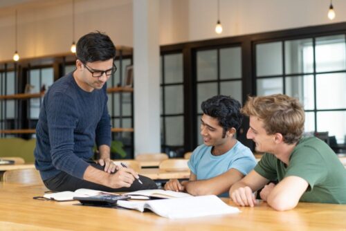 serious-teacher-checking-assignment-two-students-250kb serious-teacher-checking-assignment-two-students-250kb